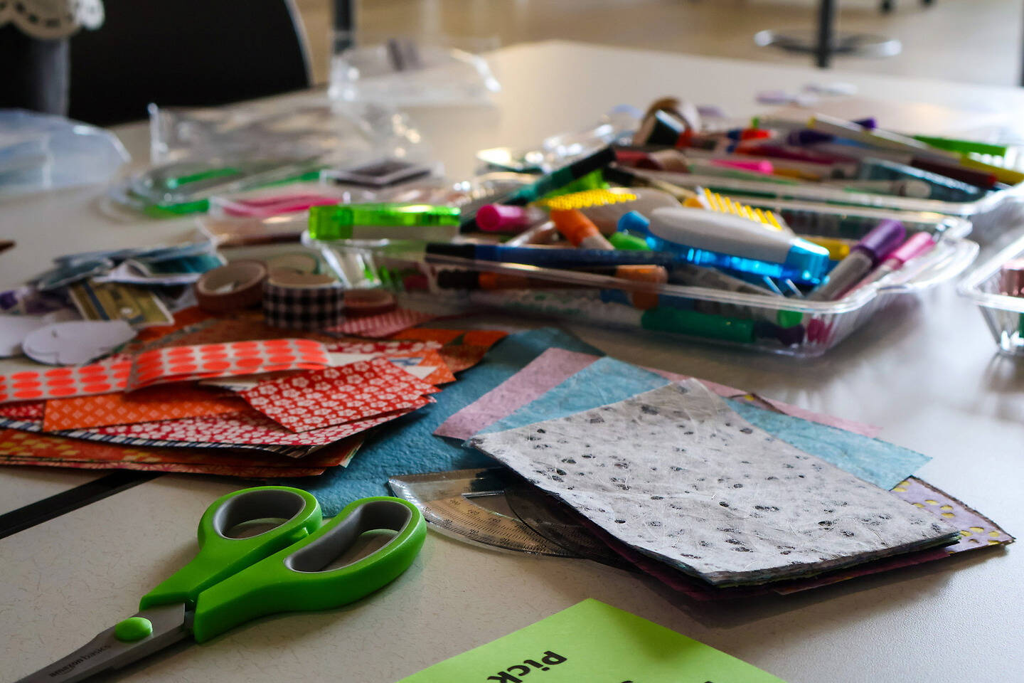 A cluttered craft table filled with colorful paper scraps, scissors, markers, and other art supplies.